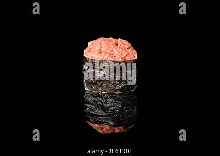 Einzelner scharf gewürzter Thunfisch Gunkan Maki Sushi mit Nori-Algenboot gefüllt mit gewürztem rohen Thunfisch, isoliert auf schwarzem Hintergrund mit Spiegelreflektion. Stockfoto