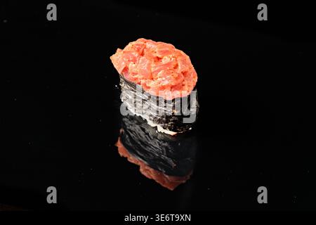Einzelner scharf gewürzter Thunfisch Gunkan Maki Sushi mit Nori-Algenboot gefüllt mit gewürztem rohen Thunfisch, isoliert auf schwarzem Hintergrund mit Spiegelreflektion. Stockfoto