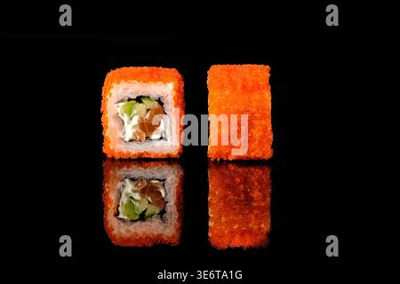 Zwei kalifornische Sushi-Brötchen, bedeckt mit orangenem tobiko fliegendem Fischrogen, mit Lachs, Frischkäse und Avocadofüllung, eines mit Querschnitt interi Stockfoto