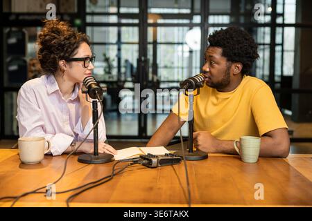 Junge Frau, die während des Interviews einem afroamerikanischen Kollegen zuhört Stockfoto