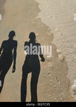 Zwei Personen laufen entlang eines Sandstrandes mit langen Schatten. Silhouette über dem Sand. Stockfoto