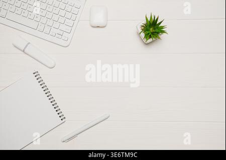 Minimaler Büroschreibtisch für Remote-Arbeiten mit weißer Tastatur, Anlage, Marker, Notebook und Ohrstöpsel auf Holz Stockfoto