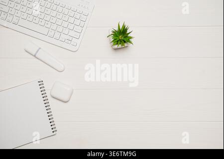 Minimaler Büroschreibtisch für Remote-Arbeiten mit weißer Tastatur, Anlage, Marker, Notebook und Ohrstöpsel auf Holz Stockfoto
