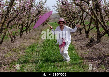 Frau genießt Frühling in blühendem Pfirsichgarten mit Schirm Stockfoto