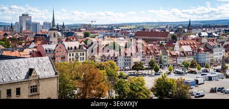 Panoramablick auf eine historische europäische Stadt mit roten Ziegeldächern, Kirchtürmen, Stadtplatz und umliegendem Grün unter teilweise bewölktem Himmel. Stockfoto