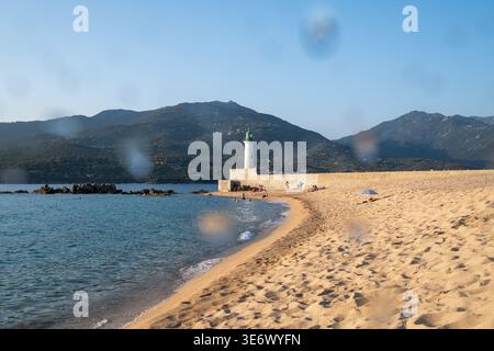 Die Menschen sitzen und entspannen am Sandstrand in der Nähe eines Leuchtturms und des Meeres in Propriano, Korsika, Frankreich, 7. August 2024. Propriano ist eine kleine Hafenstadt an der t Stockfoto