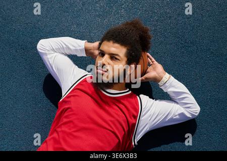 Ein energiegeladener junger Mann spielt Basketball auf einem Platz im Freien, während er die Sonnenstrahlen aufsaugt Stockfoto