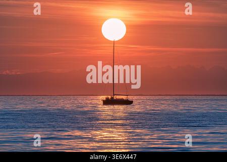 Ein Segelboot schwimmt während eines lebhaften Sonnenuntergangs auf ruhigem Wasser Stockfoto