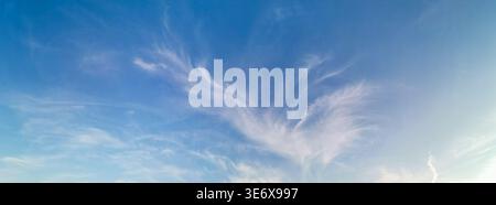 Ein weitläufiger blauer Himmel mit weichen, schimmernden Wolken, die vom warmen Licht der untergehenden Sonne beleuchtet werden, schafft eine ruhige Szene, die das Beau hervorhebt Stockfoto