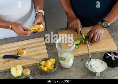 Afrikanisches Paar schält Bananen und schneidet Gurken zu Hause auf Holzbrettern, Mixbecher Stockfoto