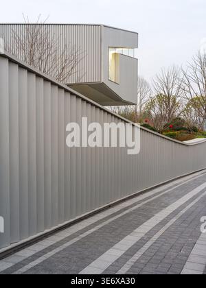 Ein dynamischer Blick auf einen gestreiften gepflasterten Gang neben einem modernen Gebäude mit einer gerippten Metallfassade und einer beeindruckenden, auskragenden Architektur Stockfoto