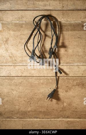 Hängende schwarze Stromkabel und Stecker an einer Wand aus schmutzigem, strukturiertem Holz mit Kopierraum, Konzept für Kabelgewirr und Organisation Stockfoto