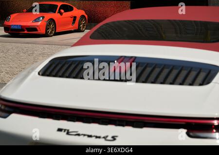 Heckdeckeldeckel und rotes Verdeck eines weißen Porsche 911 Carrera 4S mit orangefarbenem Porsche 718 im Hintergrund, Shanghai, China, Asien. Stockfoto