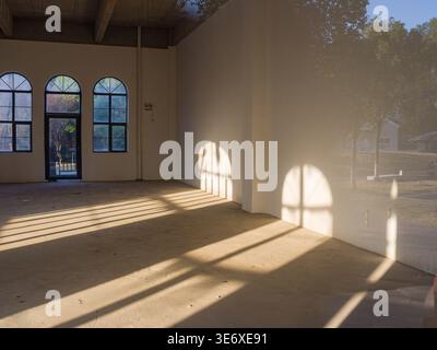 Leerer überdachter Außenflur mit Bogenfenstern und Türen, die unterschiedliche geometrische und bogenförmige Schatten auf einen glatten Betonboden unter dem Dach werfen Stockfoto