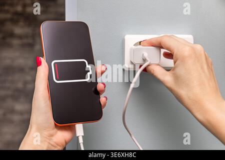 Nahaufnahme einer Frauenhände, die ein Smartphone über ein Kabel und einen USB-Anschluss aufladen. Stockfoto