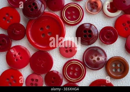 Eine Sammlung roter Tasten in verschiedenen Größen, Formen und Oberflächen. Konzepte in Bezug auf Nähen, Mode, Handwerk, Textildesign und Kreativität. Stockfoto