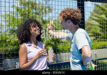Diverse Paare, die sich in Sportbekleidung auf den Tennisplatz lehnen, Frau mit Flasche, Mann mit Tennisball Stockfoto
