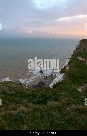 Vertikale Komposition einer markanten Küstenszene mit einem klassischen rot-weißen Leuchtturm am Fuße der steilen weißen Kreidefelsen. Stockfoto