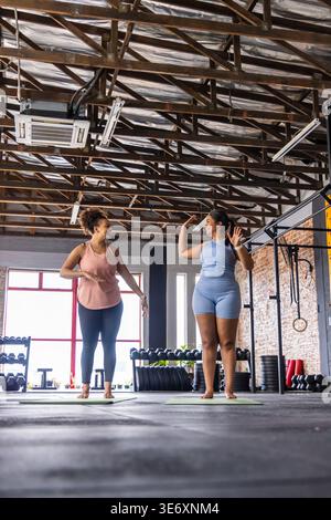 Zwei afroamerikanische Frauen stehen auf grünen Trainingsmatten im Fitnessstudio, begrüßen und aufwärmen Stockfoto