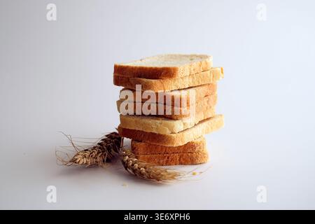 Geschnittenes weißes Toastbrot und Weizenohren auf weißem Hintergrund. Stockfoto