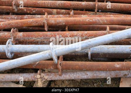 Verwitterte Industriekontrollen stapeln sich auf einem Bauplatz. Robuste Stahlstützen mit sichtbarer Oxidation und Flanschen, organisiert für Sto Stockfoto