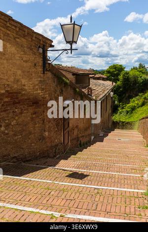 Leere, enge Backsteinstraße mit traditioneller Architektur und Laterne im historischen Zentrum von Siena, Toskana, Italien Stockfoto