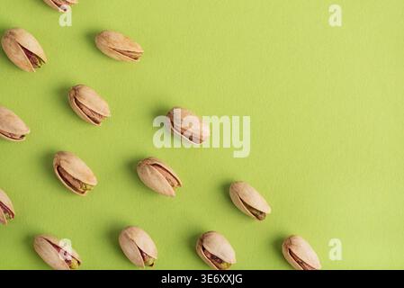 Minimalistisches Muster mit Pistazien in einem diagonalen Raster auf einem lebhaften grünen Hintergrund. Stockfoto