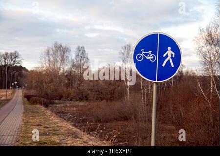 Das Schild zeigt Fahrrad- und Fußgängersymbole entlang eines Weges an Bäumen im Abendlicht Stockfoto