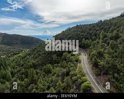 Luftaufnahme der gewundenen Bergstraße, die sich durch dichten grünen Wald im Hochland von Arizona unter blauem Himmel mit weißen Wolken an einem klaren Tag kurvt. Stockfoto