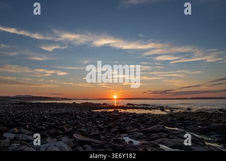 Sonnenuntergang über der felsigen Küste mit orangefarbenem Himmel und glühender Sonne, die sich auf ruhigem Wasser im Acadia Nationalpark an der Küste von Maine an einem ruhigen Abend spiegelt Stockfoto
