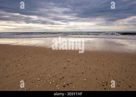 Blick auf Meereswellen und reflektierenden nassen Sand unter dramatischem bewölktem Himmel am Long Island Beach, New York, USA. Stockfoto