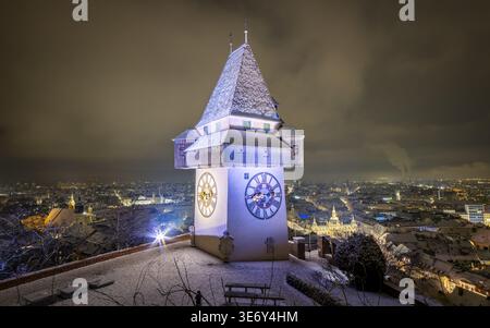 Blick auf den berühmten Uhrturm, den Uhrturm, der majestätisch gegen den Dämmerhimmel steht und einen warmen Glanz über die schneebedeckte Stadt Graz, Styr, wirft Stockfoto