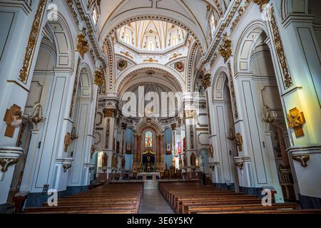 Ein großer Blick auf das neobarocke Innere der Kirche von Altea. Weiße Wände sind mit eleganten Golddekoren, majestätischen Bögen und einer hellen Kuppel verziert. Stockfoto