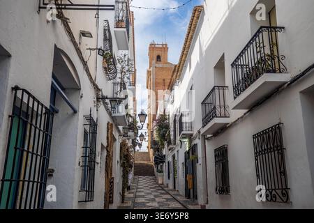 Der vertikale Blick auf eine enge Straße in Altea bietet weiße Häuser mit schmiedeeisernen Balkonen und einem dekorativen Mosaikpflaster. An der Spitze des Stai Stockfoto