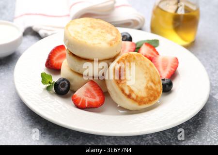 Köstliche Hüttenkäse-Pfannkuchen mit Beeren, Minze und Honig auf grauem Tisch, Nahaufnahme Stockfoto