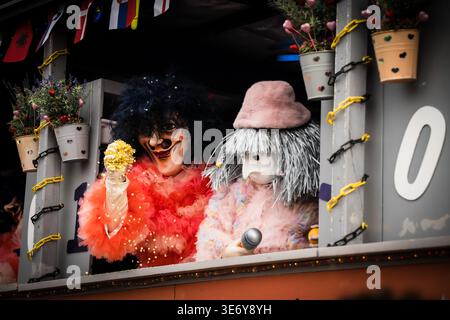 Basel, Schweiz - 10. März 2025: Blick auf zwei maskierte Figuren in leuchtend roten und zarten rosa Kostümen, die von einem dekorierten Wagen mit geschmückter Dekoration hervorblicken Stockfoto