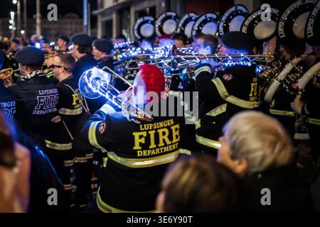 Basel, Schweiz - 10. März 2025: Blick auf eine lebhafte Band in dunklen Jacken mit leuchtenden Lichtern, deren Messinginstrumente gegen die nächtliche Beleuchtung leuchten Stockfoto
