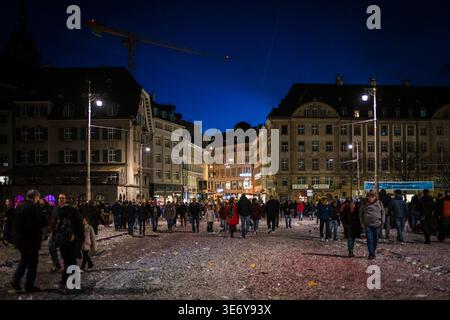 Basel, Schweiz - 10. März 2025: Blick auf einen überfüllten Platz, der unter dem Nachthimmel schimmert, mit Konfetti übersät, umgeben von der dunklen Silhouette Stockfoto