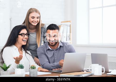 Drei begeisterte Mitarbeiter, die gute Nachrichten über Notebooks erhalten Stockfoto