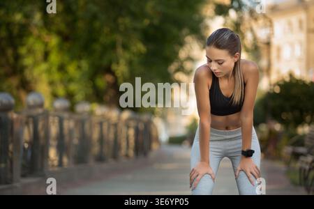 Die junge Frau macht tagsüber eine Pause, nachdem sie in einem Park gelaufen ist Stockfoto