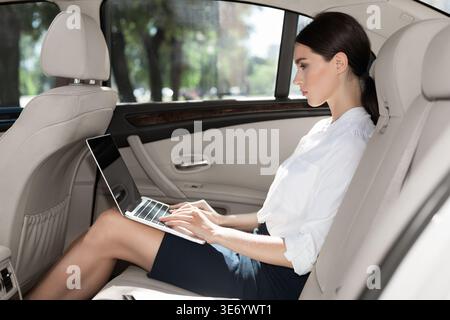 Frau mit Laptop auf dem Rücksitz im Auto Stockfoto