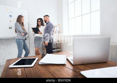 Laptop und Tablet am Arbeitsplatz mit Büroteam im Hintergrund Stockfoto