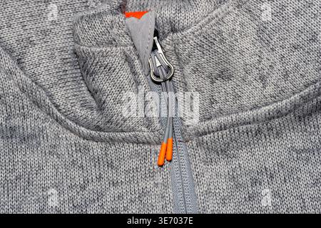 Grau meliertes Strickmaterial mit detailliertem Reißverschluss und orangefarbenen Akzenten Stockfoto