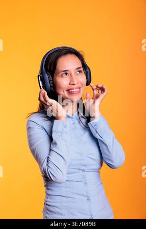 Fröhliche philippinische Frau, die Musik hört und tanzt, genießt Freizeit im Studio auf gelbem Hintergrund. Attraktives Modell mit Kopfhörern, das lustige Tanzbewegungen zeigt. Unterhaltungskonzept Stockfoto