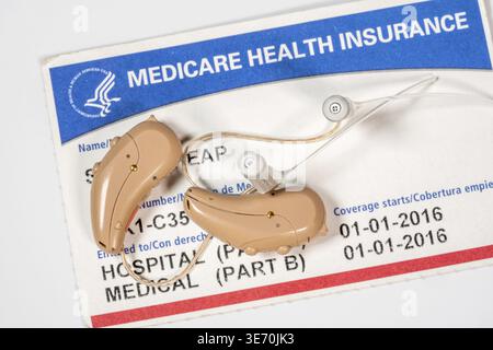 Makro-Nahaufnahme eines zusammenpassenden Paares von winzigen modernen Hörgeräten auf Medicare-Karten-Hintergrund, da die Abdeckung verbessert wird Stockfoto