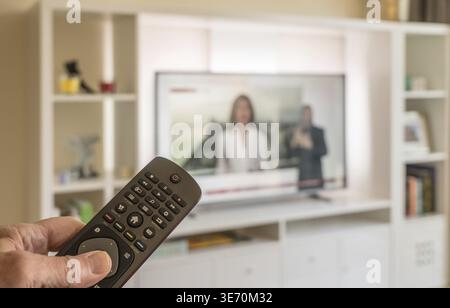 Ältere Männer halten Fernbedienung in hellem, modernem Apartment mit Großbildfernseher Stockfoto