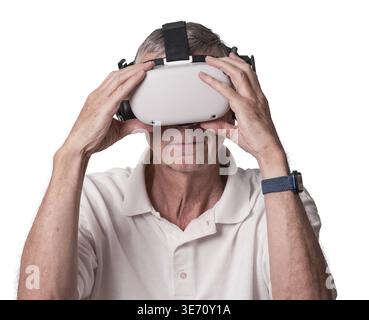 Älterer Erwachsener, der sein Virtual-Reality-Headset hält, während er eine Szene im Metaverse erkundet Stockfoto