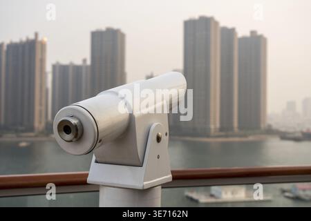 Optisches Metallteleskop an Deck des Kreuzfahrtschiffes, das nebelige Gebäude von Qingdao aussieht Stockfoto