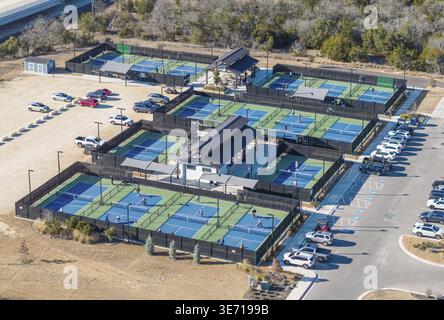 Blick aus der Vogelperspektive auf einen pulsierenden Pickleball-Komplex, zahlreiche Plätze mit Spielern, umgeben von großen Parkplätzen und üppigem Grün Stockfoto