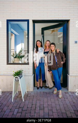 Drei lächelnde kleine Geschäftsinhaberinnen stehen in ihrer Boutique Stockfoto